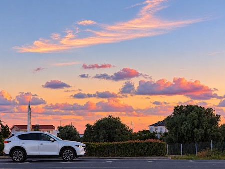 A beautiful pastel sunset with soft pink and orange clouds stretching across the evening sky above a quiet suburban street in Cyprus.