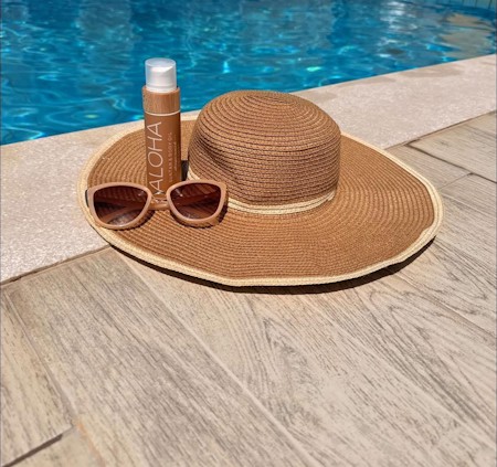 A stylish summer scene featuring a chic straw sun hat, sunglasses, and body oil by the poolside. A perfect combination of relaxation, sunshine, and vacation vibes with a touch of tropical elegance